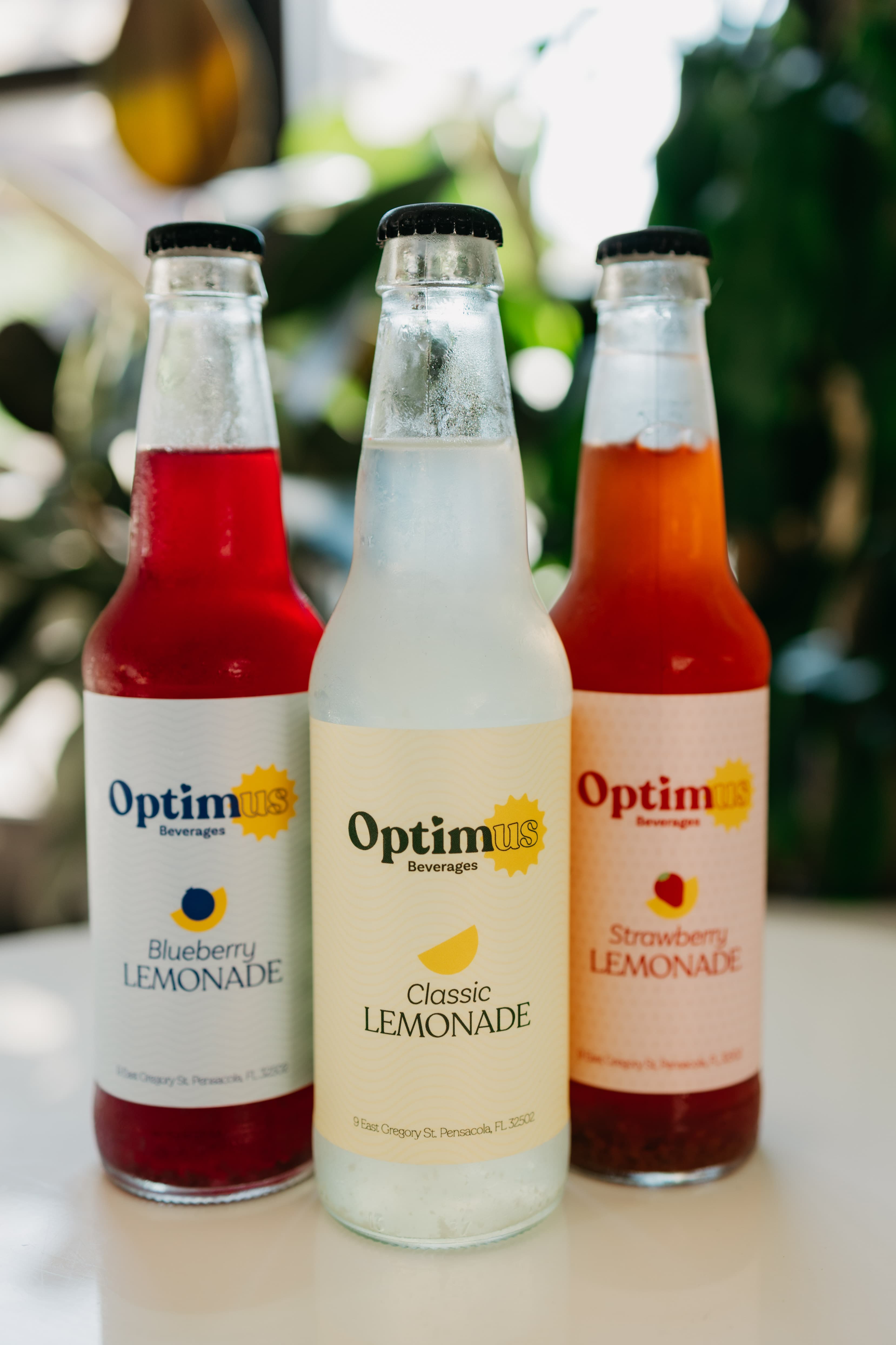 Three Optimus Beverages lemonade bottles — blueberry, classic and strawberry — lined up outdoors