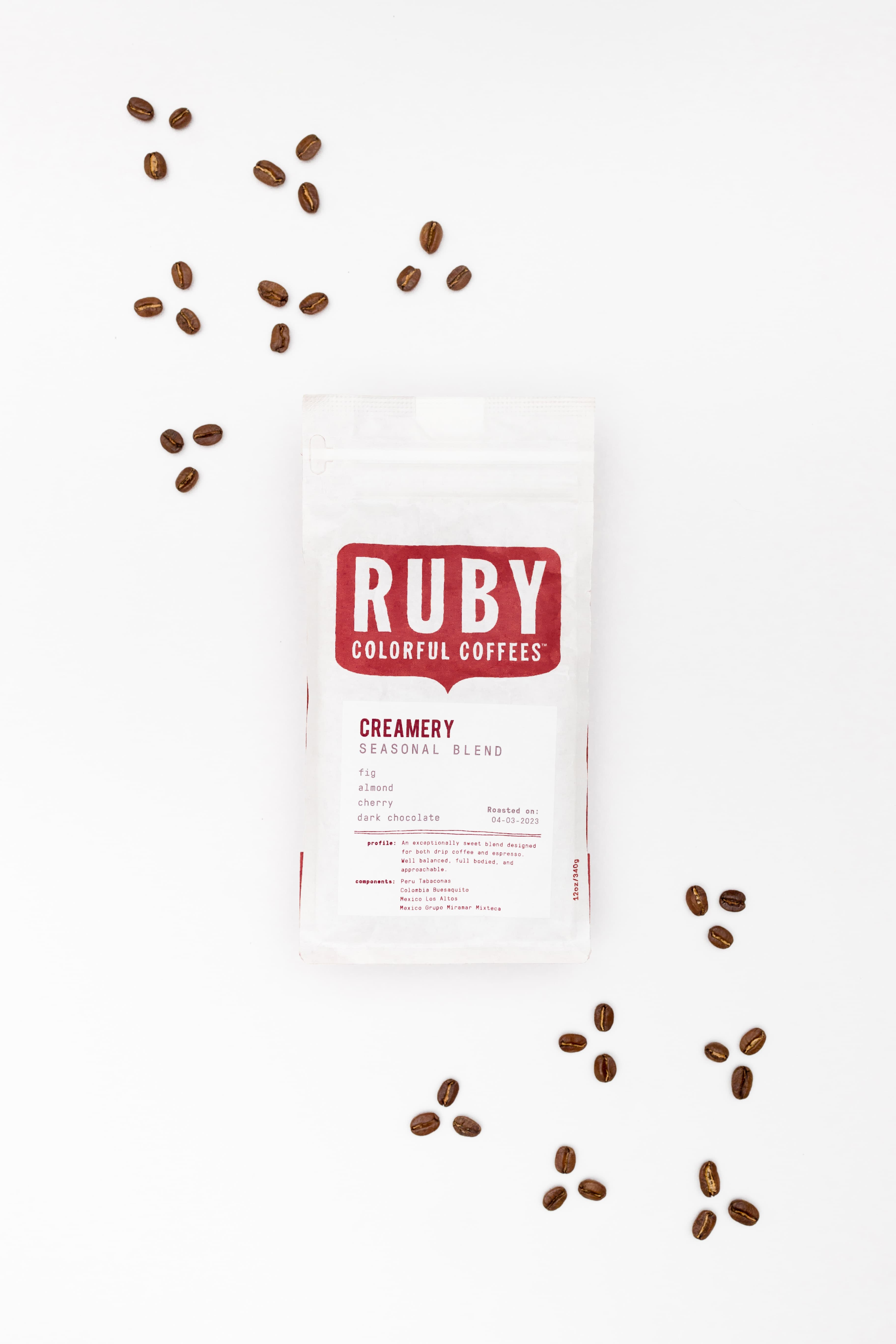 A Ruby Colorful Coffees bag standing upright with roasted beans scattered around it